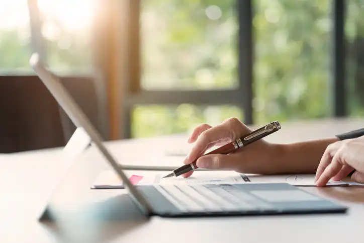 Close up of businessman or accountant hand holding pen working on laptop computer for calculate business data, accountancy document and calculator at office, business concept
